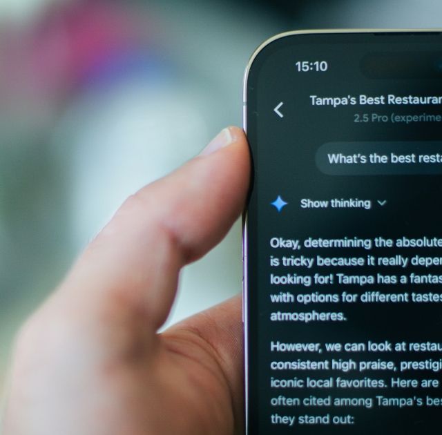 En person håller i en smartphone som visar en app för att söka restauranger i Tampa, vilket definierar ZORC:s AI-funktioner